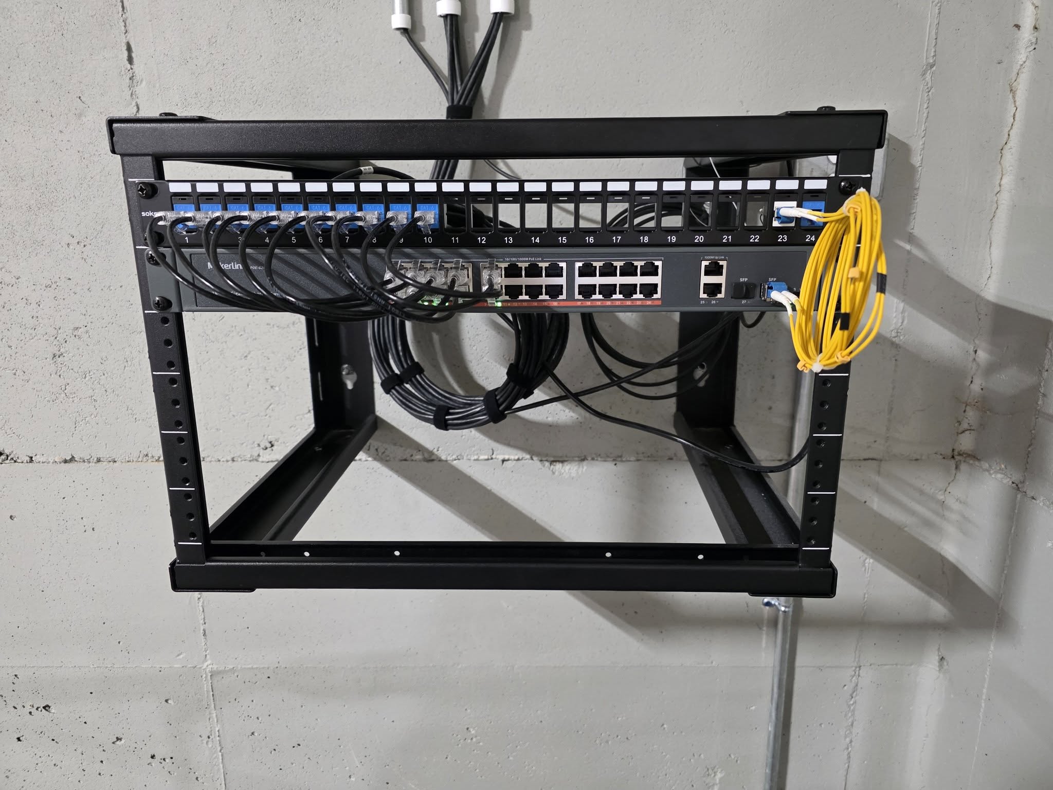 Wall-mounted open frame rack with labeled patch panel and managed PoE switch